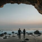 man and woman holding hands facing sea